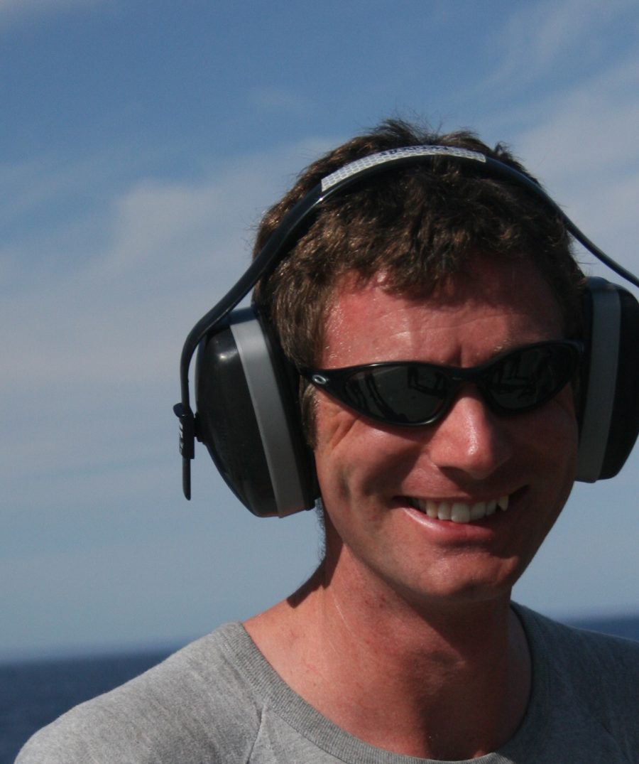 Adrian at sea, smiling, wearing ear defenders